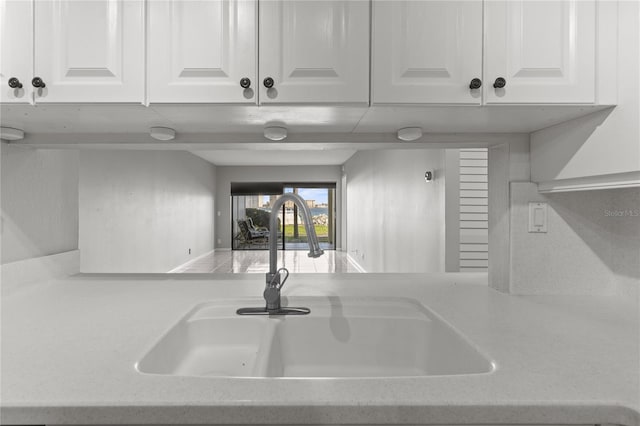 kitchen with light stone counters, white cabinetry, and sink