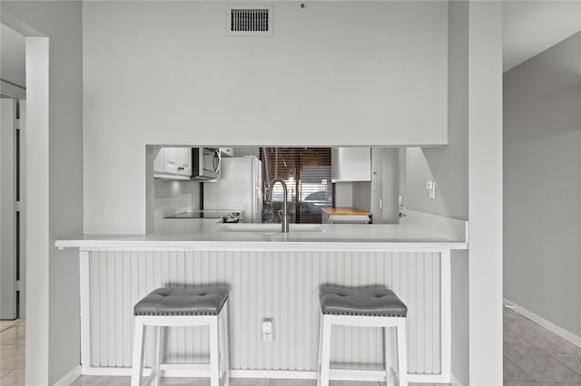 kitchen with kitchen peninsula, a breakfast bar, refrigerator, and sink