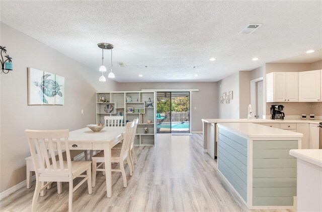 kitchen featuring white cabinets, a textured ceiling, light hardwood / wood-style floors, and hanging light fixtures