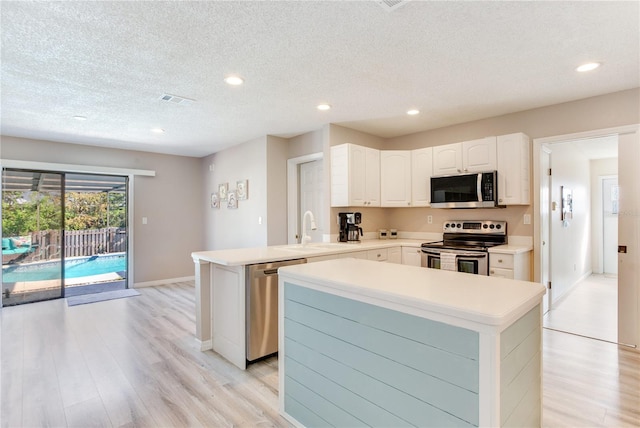 kitchen with sink, stainless steel appliances, kitchen peninsula, white cabinets, and light wood-type flooring