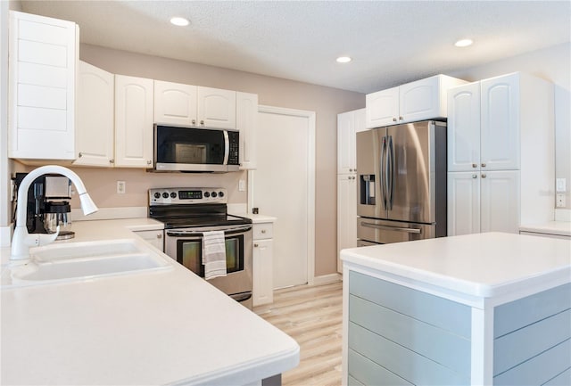 kitchen with white cabinetry, sink, a textured ceiling, appliances with stainless steel finishes, and light wood-type flooring