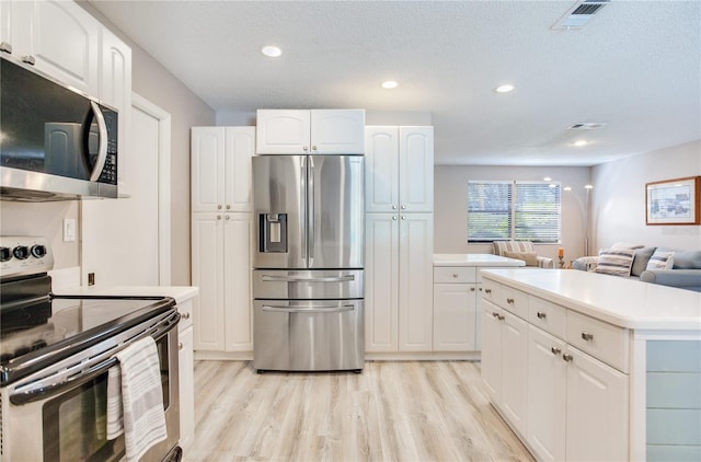 kitchen featuring appliances with stainless steel finishes, light wood-type flooring, a textured ceiling, white cabinets, and a center island