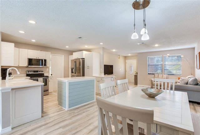 kitchen with decorative light fixtures, light wood-type flooring, sink, and appliances with stainless steel finishes