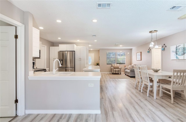 kitchen featuring decorative light fixtures, stainless steel fridge, white cabinetry, and light hardwood / wood-style flooring