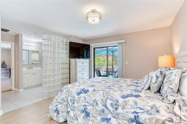 bedroom with access to exterior, light wood-type flooring, ensuite bath, and sink