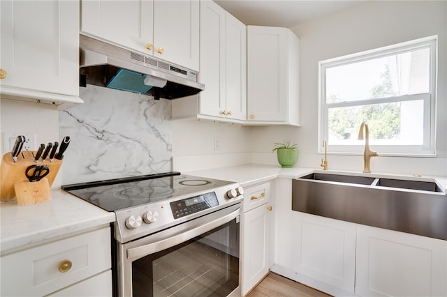 kitchen featuring stainless steel range with electric cooktop, white cabinetry, tasteful backsplash, sink, and light stone counters