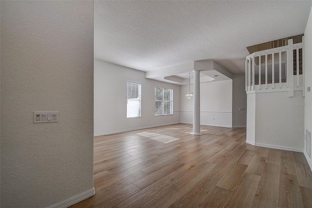 unfurnished room featuring a chandelier, light wood-type flooring, a textured ceiling, and decorative columns