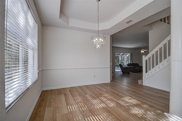 empty room with stairway, a raised ceiling, baseboards, and wood finished floors