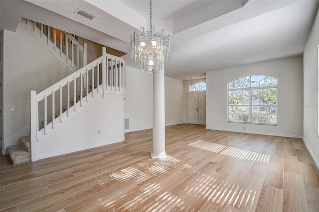 unfurnished living room with a textured ceiling, an inviting chandelier, ornate columns, and hardwood / wood-style flooring