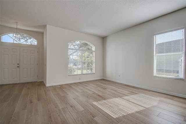 entrance foyer featuring light wood-type flooring, a textured ceiling, and an inviting chandelier