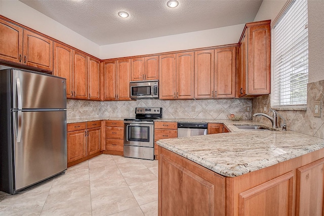 kitchen with sink, light stone countertops, appliances with stainless steel finishes, light tile patterned flooring, and kitchen peninsula