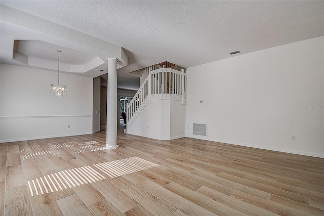 unfurnished living room featuring a tray ceiling, light wood-style flooring, decorative columns, and visible vents