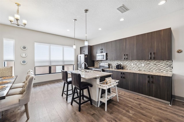 kitchen with decorative backsplash, dark brown cabinetry, stainless steel appliances, and an island with sink