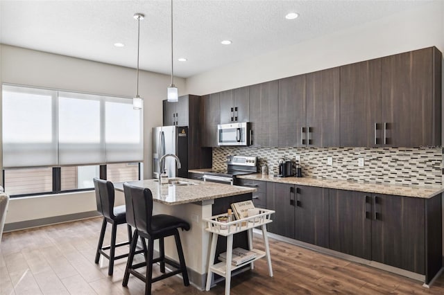 kitchen featuring backsplash, dark brown cabinets, light stone counters, and stainless steel appliances