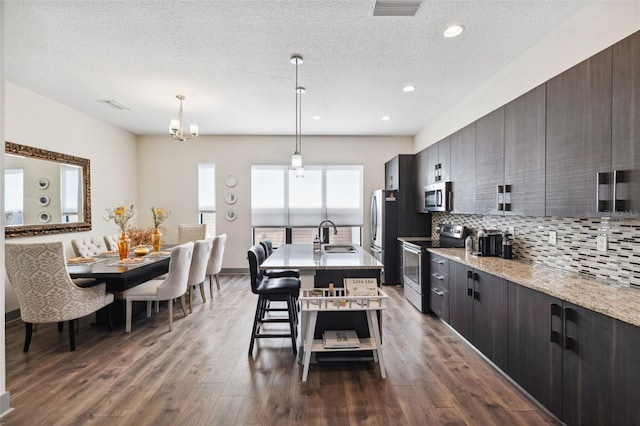 kitchen with hanging light fixtures, a kitchen breakfast bar, an island with sink, dark brown cabinets, and appliances with stainless steel finishes