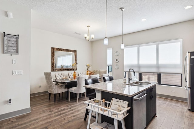 kitchen with a center island with sink, sink, hanging light fixtures, appliances with stainless steel finishes, and wood-type flooring