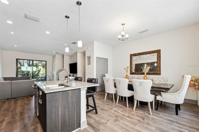 kitchen featuring sink, a center island with sink, light hardwood / wood-style flooring, a notable chandelier, and hanging light fixtures