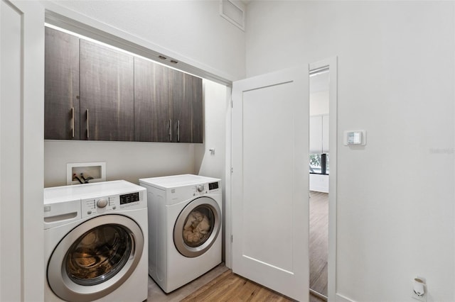 laundry room featuring washer and dryer, light wood-type flooring, and cabinets