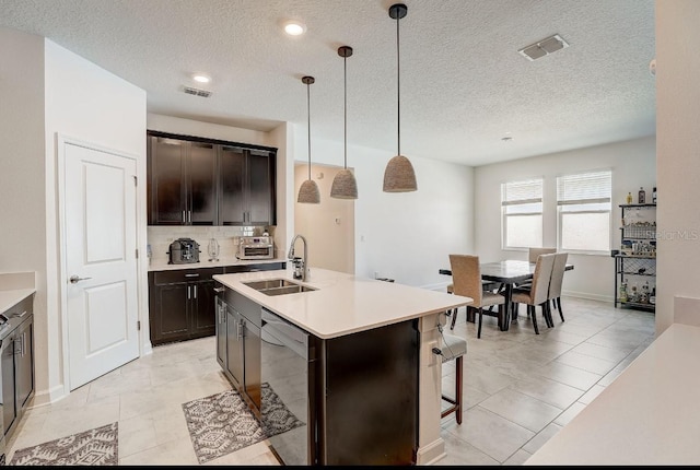 kitchen featuring dark brown cabinetry, sink, pendant lighting, dishwasher, and an island with sink