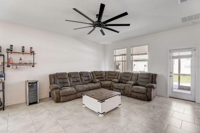 living room featuring ceiling fan, light tile patterned flooring, a textured ceiling, and wine cooler