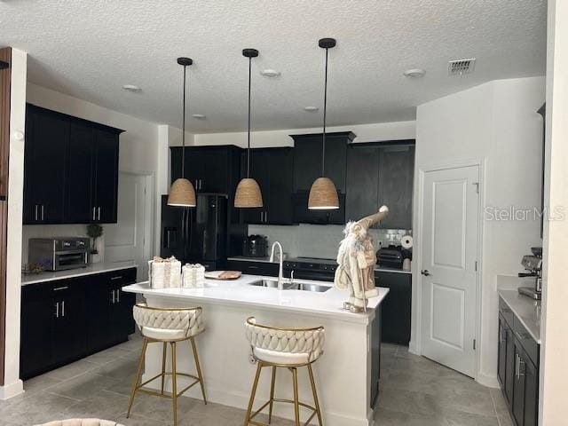 kitchen featuring a kitchen bar, black refrigerator with ice dispenser, a kitchen island with sink, sink, and hanging light fixtures