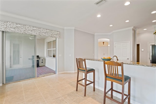 kitchen with a kitchen breakfast bar, light stone counters, ornamental molding, and light tile patterned floors