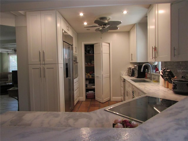 kitchen featuring backsplash, sink, ceiling fan, stovetop, and white cabinetry