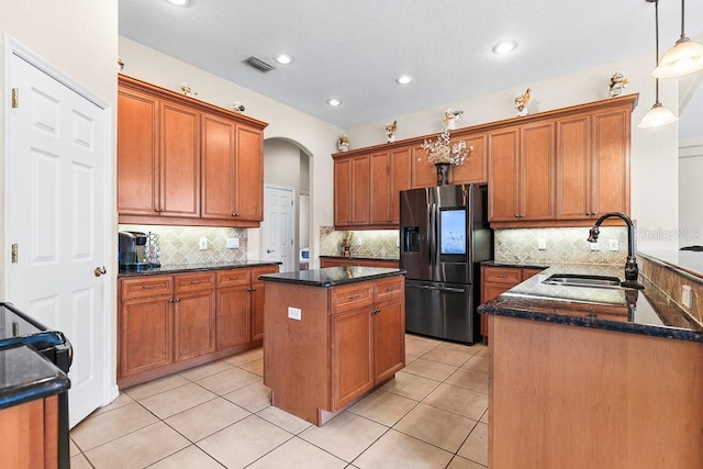 kitchen featuring pendant lighting, a center island, sink, stainless steel fridge, and dark stone countertops