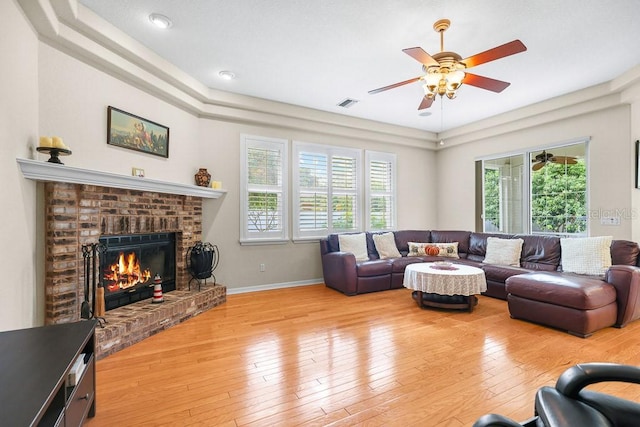 living room featuring ceiling fan, light wood-type flooring, and a brick fireplace