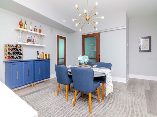 dining area with bar area, light hardwood / wood-style floors, and a chandelier