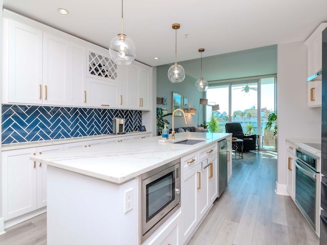 kitchen with stainless steel appliances, sink, pendant lighting, a center island with sink, and white cabinets