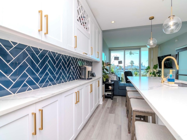 kitchen featuring hanging light fixtures, light stone countertops, tasteful backsplash, light hardwood / wood-style floors, and white cabinetry