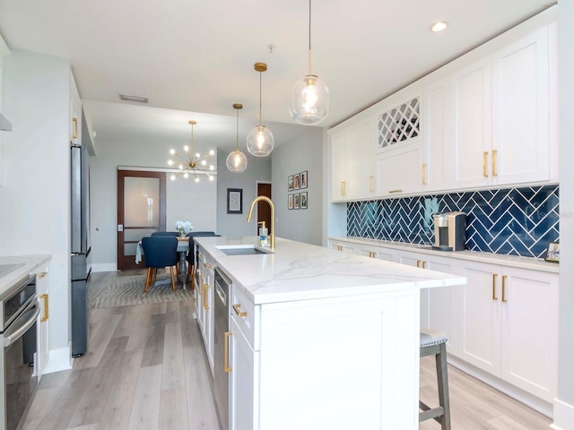 kitchen with white cabinetry, hanging light fixtures, an island with sink, appliances with stainless steel finishes, and light wood-type flooring