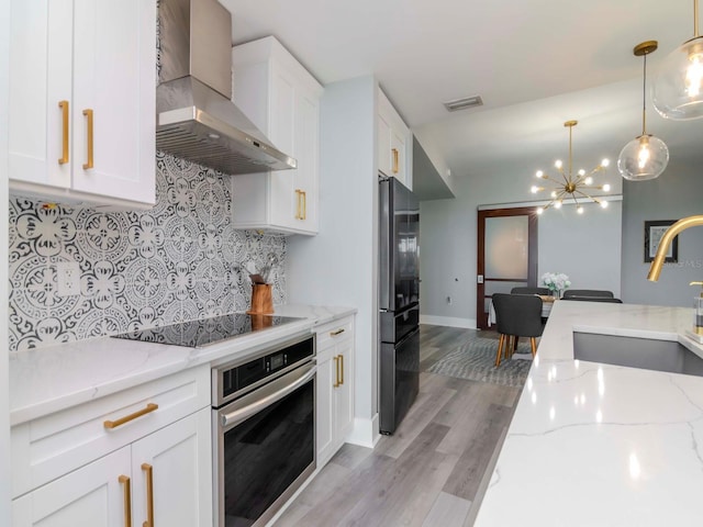 kitchen with black appliances, white cabinets, wall chimney exhaust hood, light hardwood / wood-style floors, and light stone counters