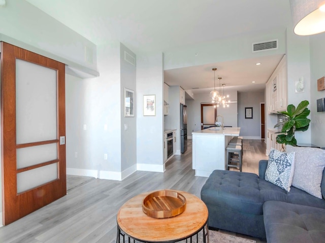 living room with light wood-type flooring, a notable chandelier, and sink