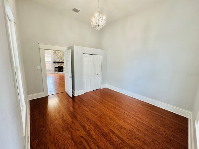 unfurnished room with a stone fireplace, dark wood-type flooring, and a notable chandelier