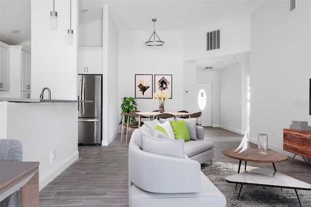 living area featuring wood finished floors, visible vents, a towering ceiling, and baseboards