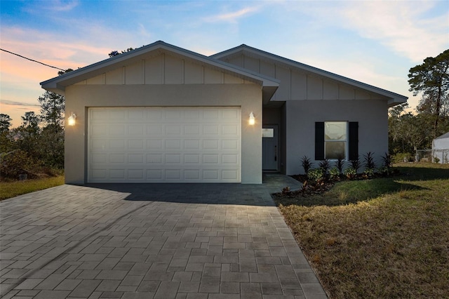 single story home featuring a lawn, board and batten siding, decorative driveway, and a garage