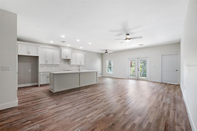 kitchen with ceiling fan, white cabinetry, hardwood / wood-style floors, a center island with sink, and french doors