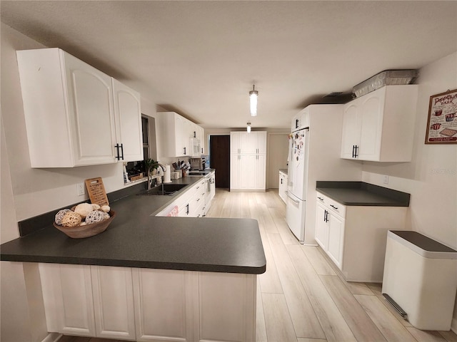 kitchen featuring kitchen peninsula, light wood-type flooring, white appliances, sink, and white cabinets