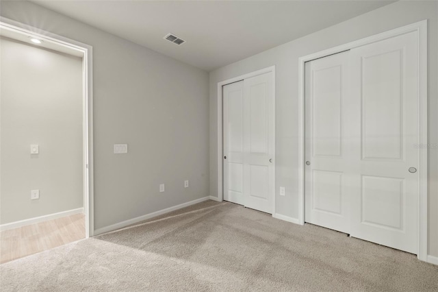 unfurnished bedroom featuring two closets and light colored carpet