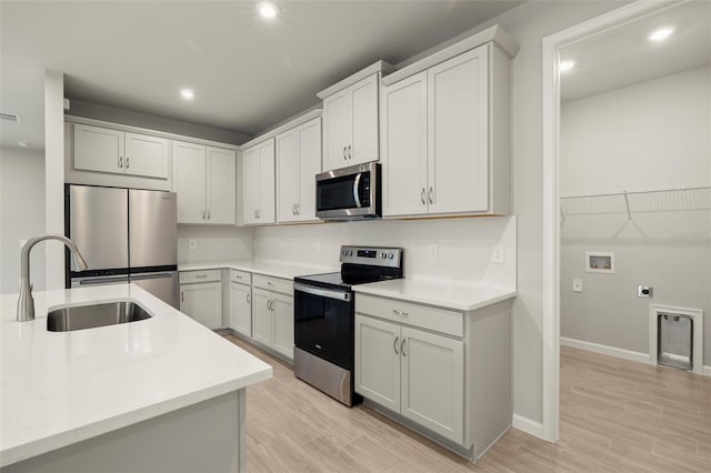 kitchen with appliances with stainless steel finishes, sink, white cabinets, and light wood-type flooring