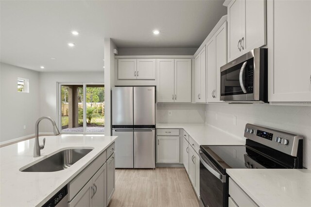 kitchen with sink, white cabinets, light stone counters, stainless steel appliances, and light hardwood / wood-style flooring