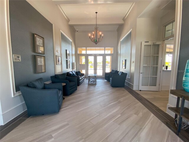 living room with light hardwood / wood-style flooring, an inviting chandelier, a towering ceiling, french doors, and beamed ceiling