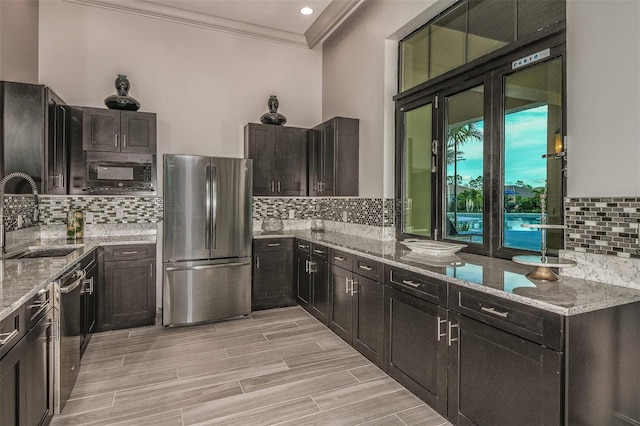 kitchen with stainless steel appliances, crown molding, light stone countertops, and sink