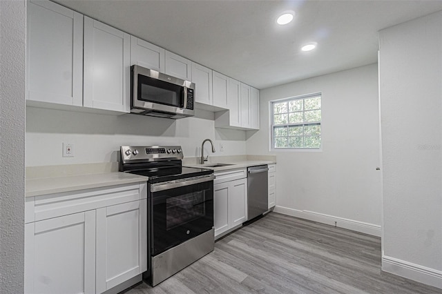 kitchen with white cabinets, light hardwood / wood-style floors, sink, and appliances with stainless steel finishes