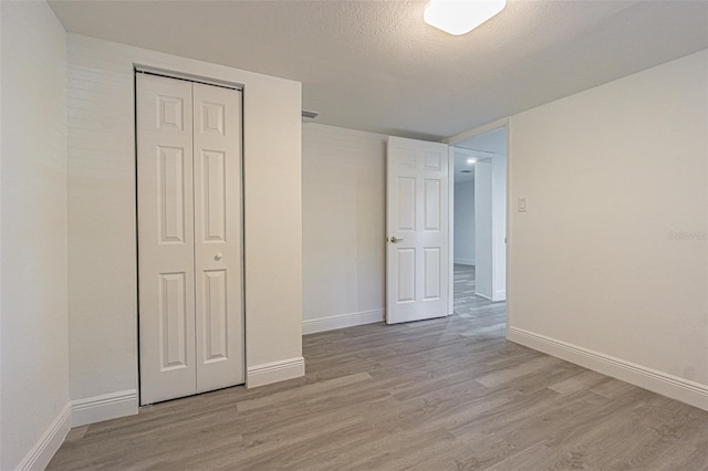 unfurnished bedroom featuring a textured ceiling, light hardwood / wood-style floors, and a closet