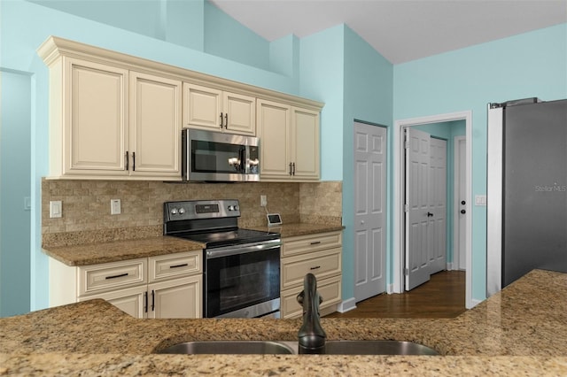 kitchen featuring cream cabinets, light stone counters, appliances with stainless steel finishes, and a sink