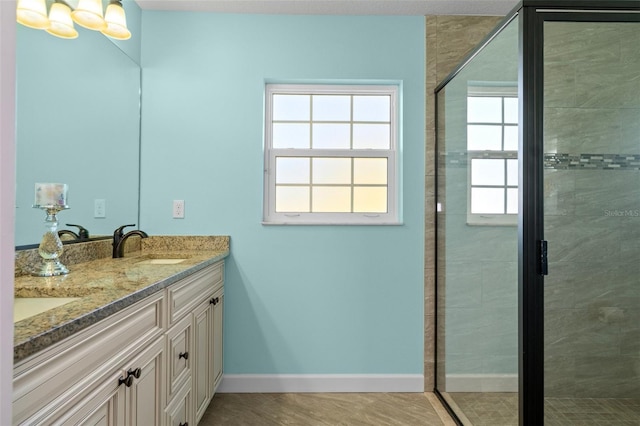 bathroom with baseboards, double vanity, a stall shower, a notable chandelier, and a sink