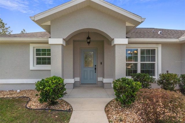 entrance to property featuring stucco siding and roof with shingles